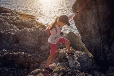 Téléchargez les photos : Jeune femme avec une corde monte au sommet dans les montagnes près de l'océan. - en image libre de droit