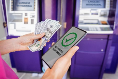 Téléchargez les photos : Jeune femme utilisant le téléphone intelligent pour retirer sans carte l'argent près du distributeur automatique de billets. - en image libre de droit