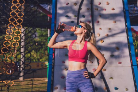 Photo for Athletic young woman drinking water after working out and climbing at the artificial rock in training camp - Royalty Free Image