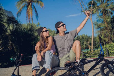 Téléchargez les photos : Jeune couple heureux avec BMX prendre selfie au skatepark. - en image libre de droit