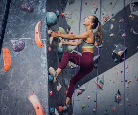 Téléchargez les photos : Une grimpeuse forte escalade un mur artificiel avec des poignées et des cordes colorées - en image libre de droit