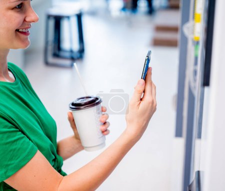 Photo for Young woman paying for coffee at vending machine using contactless method of payment. - Royalty Free Image
