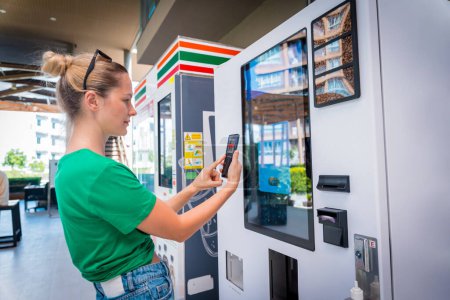 Jeune femme payant pour le café au distributeur automatique en utilisant le mode de paiement sans contact.