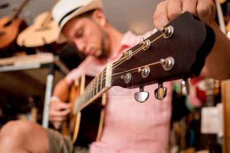 Foto de Joven músico afinando una guitarra clásica en una tienda de guitarra. - Imagen libre de derechos