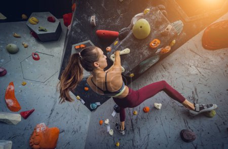 Photo for A strong female climber climbs an artificial wall with colorful grips and ropes - Royalty Free Image