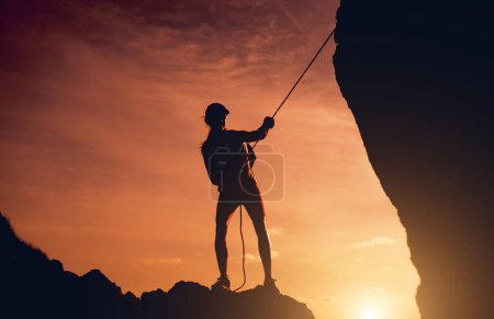 Foto de Mujer joven con una cuerda sube a la cima de las montañas cerca del océano. - Imagen libre de derechos