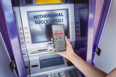 Photo for Young woman using the smart phone for cardless withdrawing the cash near the ATM. - Royalty Free Image