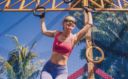 Foto de Mujer joven atlética haciendo ejercicio usando anillos gimnásticos en un campo de entrenamiento. - Imagen libre de derechos