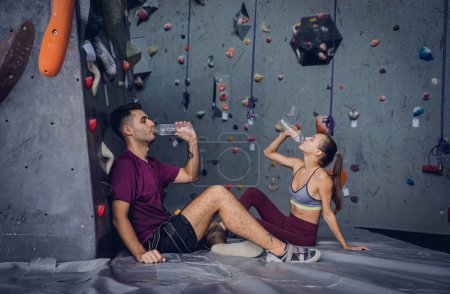 Foto de Un fuerte par de escaladores se relajan cerca de la pared artificial con pintorescos agarres y cuerdas - Imagen libre de derechos