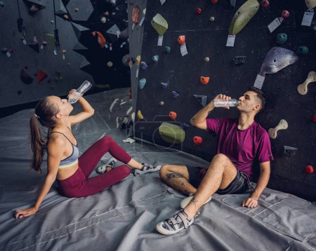 Téléchargez les photos : Un couple fort d'alpinistes se détendent près d'un mur artificiel avec des poignées et des cordes colorées - en image libre de droit