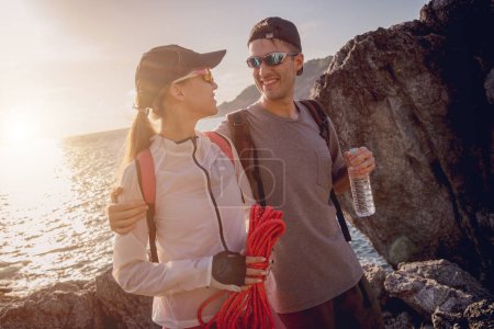 Téléchargez les photos : Jeune couple monte avec une corde au sommet dans les montagnes près de l'océan. - en image libre de droit