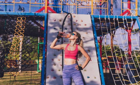 Photo for Athletic young woman drinking water after working out and climbing at the artificial rock in training camp - Royalty Free Image
