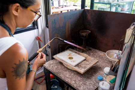 Téléchargez les photos : Bijoutier utilisant un brûleur pour façonner une pièce dans un atelier. - en image libre de droit