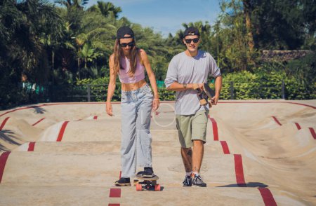 Téléchargez les photos : Jeune couple heureux avec planches à roulettes profiter du longboard au skatepark. - en image libre de droit