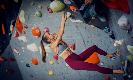 Foto de Una fuerte escaladora trepa por una pared artificial con pintorescos agarres y cuerdas - Imagen libre de derechos