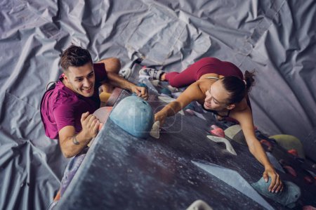 Photo for A strong couple of climbers climb an artificial wall with colorful grips and ropes - Royalty Free Image