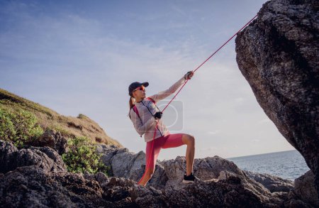 Téléchargez les photos : Jeune femme avec une corde monte au sommet dans les montagnes près de l'océan. - en image libre de droit