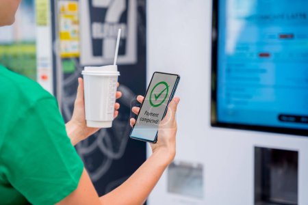 Téléchargez les photos : Jeune femme payant pour le café au distributeur automatique en utilisant le mode de paiement sans contact. - en image libre de droit