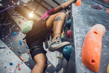 Foto de Un fuerte escalador macho trepa una pared artificial con pintorescos agarres y cuerdas - Imagen libre de derechos