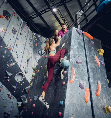 Téléchargez les photos : Un couple fort d'alpinistes escalade un mur artificiel avec des poignées et des cordes colorées - en image libre de droit