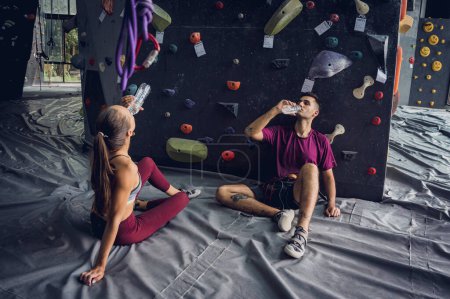 Photo for A strong couple of climbers relax near artificial wall with colorful grips and ropes - Royalty Free Image