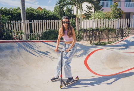 Téléchargez les photos : Heureuse jeune femme avec scooter profiter de l'équitation au skatepark. - en image libre de droit
