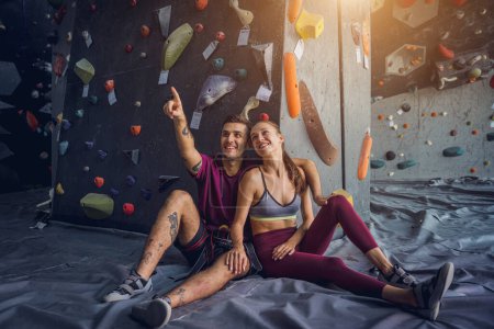 Téléchargez les photos : Un couple fort d'alpinistes contre un mur artificiel avec des poignées et des cordes colorées - en image libre de droit