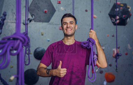 Foto de Un fuerte escalador masculino contra una pared artificial con pintorescos agarres y cuerdas - Imagen libre de derechos