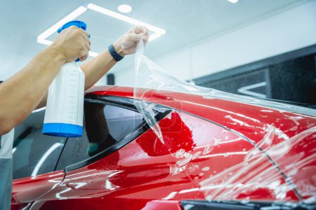 Photo for Worker in car service sprays water on the car before applying an protective film - Royalty Free Image