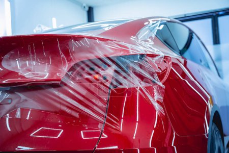 Téléchargez les photos : Le processus d'installation du film de protection sur la nouvelle voiture rouge - en image libre de droit