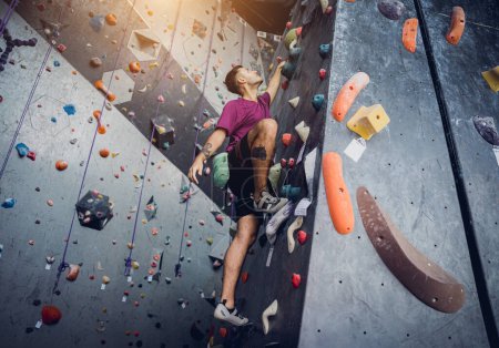 Photo for A strong male climber climbs an artificial wall with colorful grips and ropes - Royalty Free Image