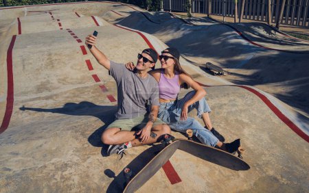 Téléchargez les photos : Jeune couple heureux avec skateboards prendre selfie au skatepark. - en image libre de droit