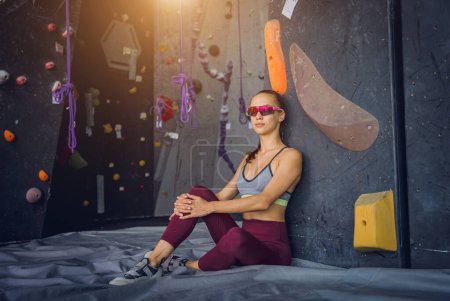 Photo for A strong female climber against an artificial wall with colorful grips and ropes - Royalty Free Image