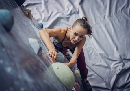 Photo for A strong female climber climbs an artificial wall with colorful grips and ropes - Royalty Free Image