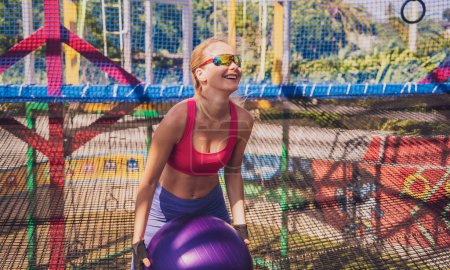 Foto de Mujer joven atlética haciendo ejercicio usando fitball en un campo de entrenamiento. - Imagen libre de derechos