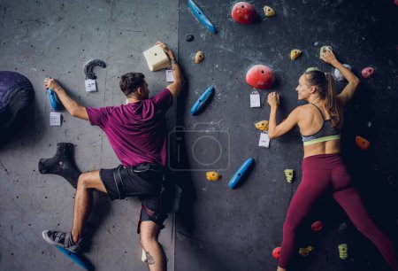 Photo for A strong couple of climbers climb an artificial wall with colorful grips and ropes - Royalty Free Image