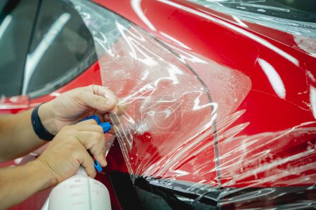 Photo for Worker in car service sprays water on the car before applying an protective film - Royalty Free Image