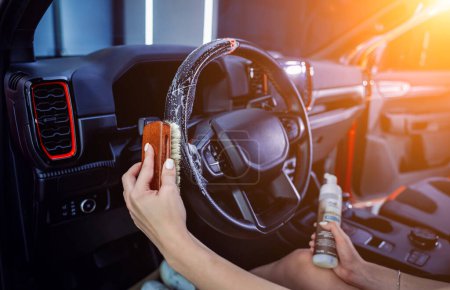 Photo for Young woman cleaning the steering wheel of car using a special brush with foam. - Royalty Free Image