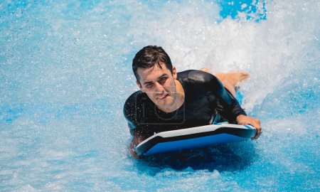 Photo for Young man surfing on a wave simulator at a water amusement park. - Royalty Free Image