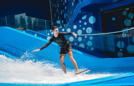 Foto de Joven surfeando con entrenador en un simulador de olas en un parque de atracciones acuático. - Imagen libre de derechos