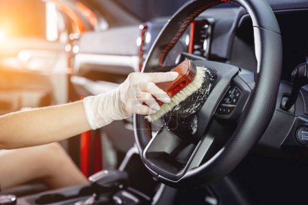 Téléchargez les photos : Jeune femme nettoyer le volant de la voiture à l'aide d'une brosse spéciale avec de la mousse. - en image libre de droit