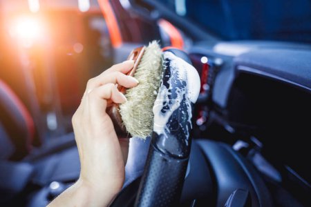 Foto de Mujer joven limpiando el volante del coche con un cepillo especial con espuma. - Imagen libre de derechos