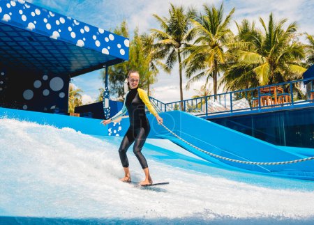 Foto de Hermosa joven surfeando con entrenador en un simulador de olas en un parque de atracciones acuático. - Imagen libre de derechos