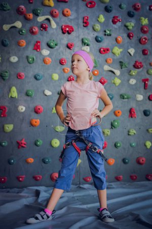 Téléchargez les photos : Un bébé grimpeur fort posant pour photographe au mur artificiel - en image libre de droit