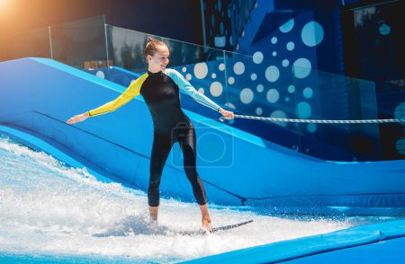 Photo for Beautiful young woman surfing on a wave simulator at a water amusement park. - Royalty Free Image