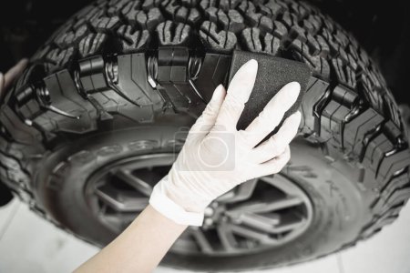 Photo for Professional car service worker polishing car tires with black sponge. - Royalty Free Image