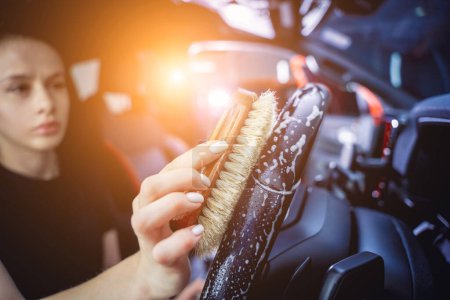 Téléchargez les photos : Jeune femme nettoyer le volant de la voiture à l'aide d'une brosse spéciale avec de la mousse. - en image libre de droit