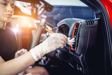 Téléchargez les photos : Jeune femme nettoyage de l'intérieur de la voiture à l'aide d'une brosse spéciale avec mousse. - en image libre de droit