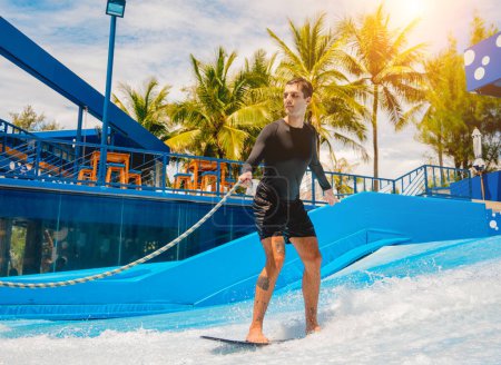 Téléchargez les photos : Jeune homme surfant sur un simulateur de vagues dans un parc d'attractions aquatiques. - en image libre de droit