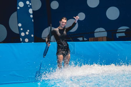 Téléchargez les photos : Jeune homme surfant sur un simulateur de vagues dans un parc d'attractions aquatiques. - en image libre de droit